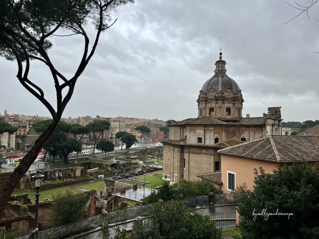 Vista panorámica desde una altura de las ruinas del Foro Romano bajo un cielo nublado. En primer plano destaca la cúpula de la Iglesia de los Santos Luca y Martina