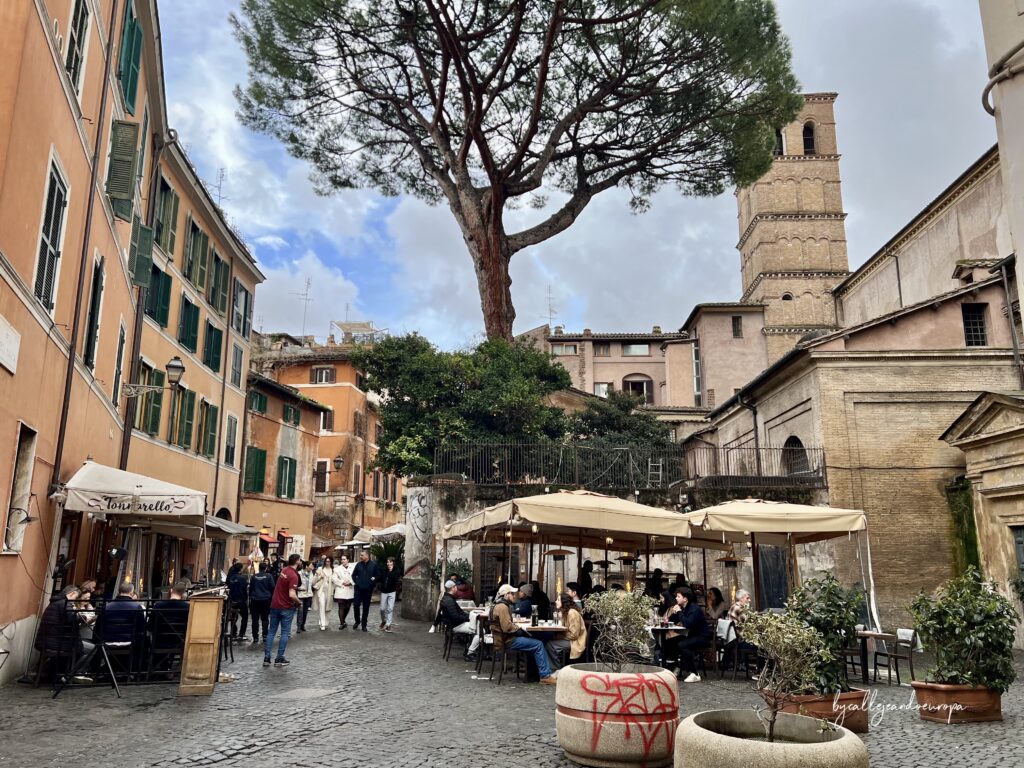 Terraza del restaurante Tonnarello en una calle de Trastevere en Roma, con edificios de tonos ocres y gente paseando en una tarde nublada.