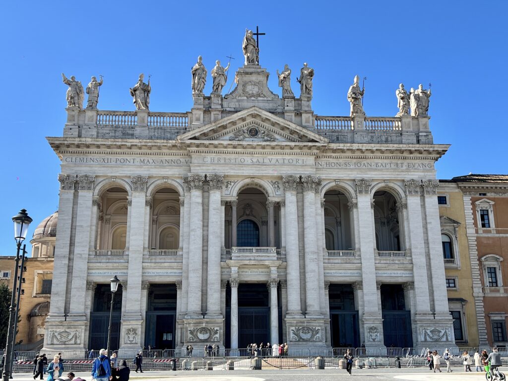 Fachada barroca de la Archibasílica de San Juan de Letrán en Roma, con sus columnas monumentales y estatuas de santos en el ático bajo un cielo azul despejado