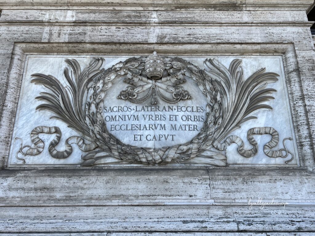 Inscripción en mármol de la Archibasílica de San Juan de Letrán en Roma, rodeada por una corona de laurel, las llaves de San Pedro y la tiara papal