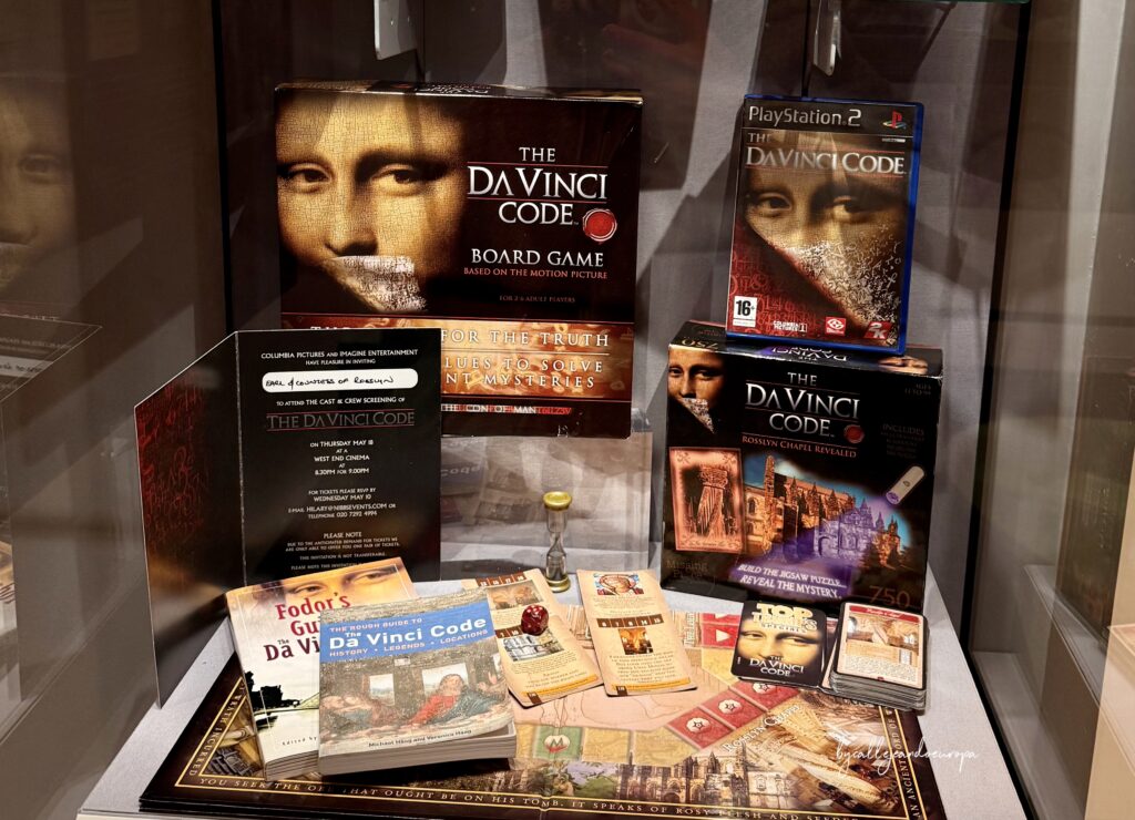 Vitrina de exhibición con productos de El Código Da Vinci, incluyendo el juego de mesa, el videojuego de PlayStation 2, libros y una invitación de cine