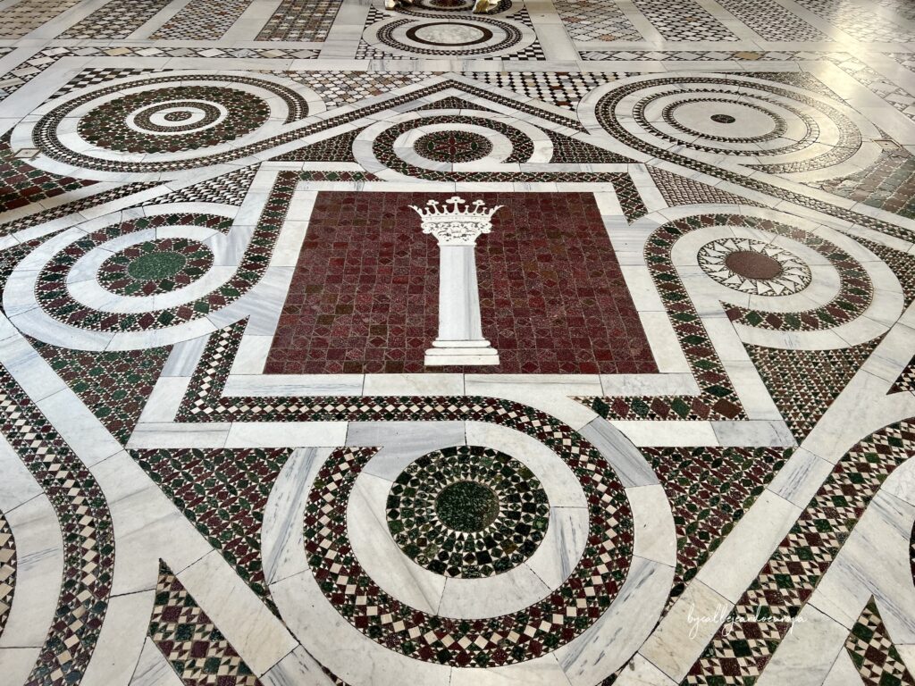 Detalle del pavimento cosmatesco de la Archibasílica de San Juan de Letrán en Roma, con mosaicos geométricos de mármol y el emblema de la columna coronada