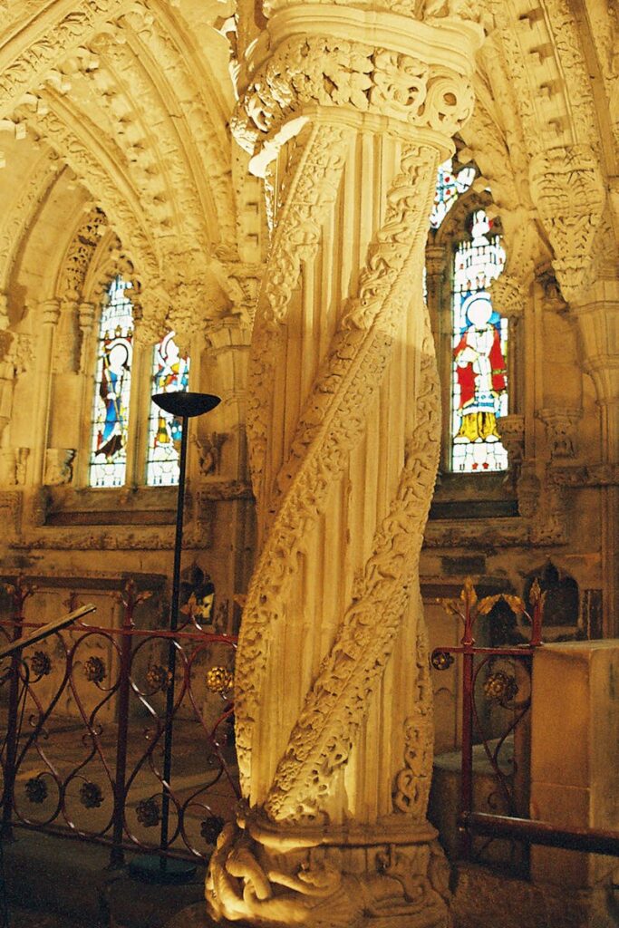 A detailed carved pillar within a historic chapel with stained glass windows.