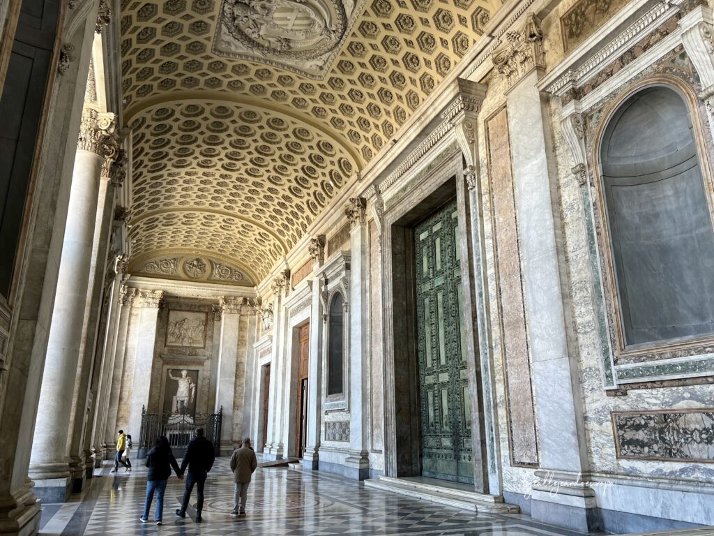 Pórtico monumental de la Archibasílica de San Juan de Letrán con techos de casetones dorados, suelos de mármol geométrico y las grandes puertas de bronce de la Curia Julia