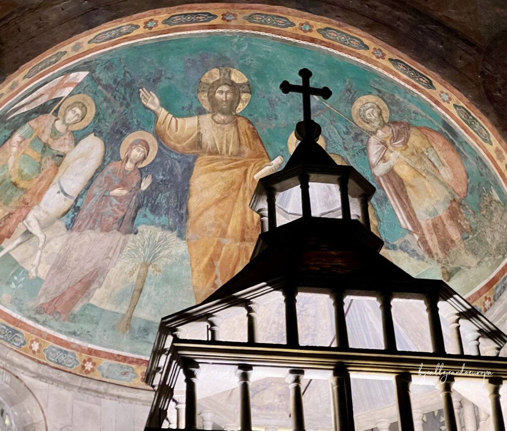 Fresco medieval en el ábside de la Iglesia de San Giorgio al Velabro en Roma, mostrando a Cristo junto a San Jorge y la Virgen María tras un copón de madera.