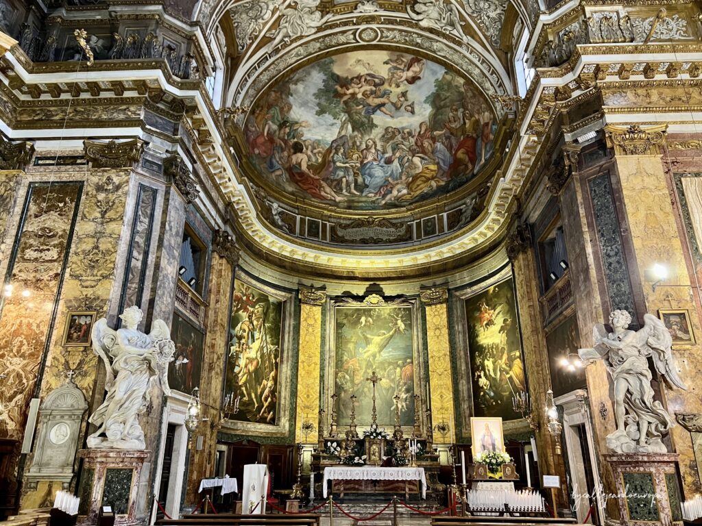Interior barroco de la basílica con un altar decorado con pinturas doradas, un fresco en la cúpula del ábside y dos grandes esculturas de ángeles de mármol blanco a los lados.