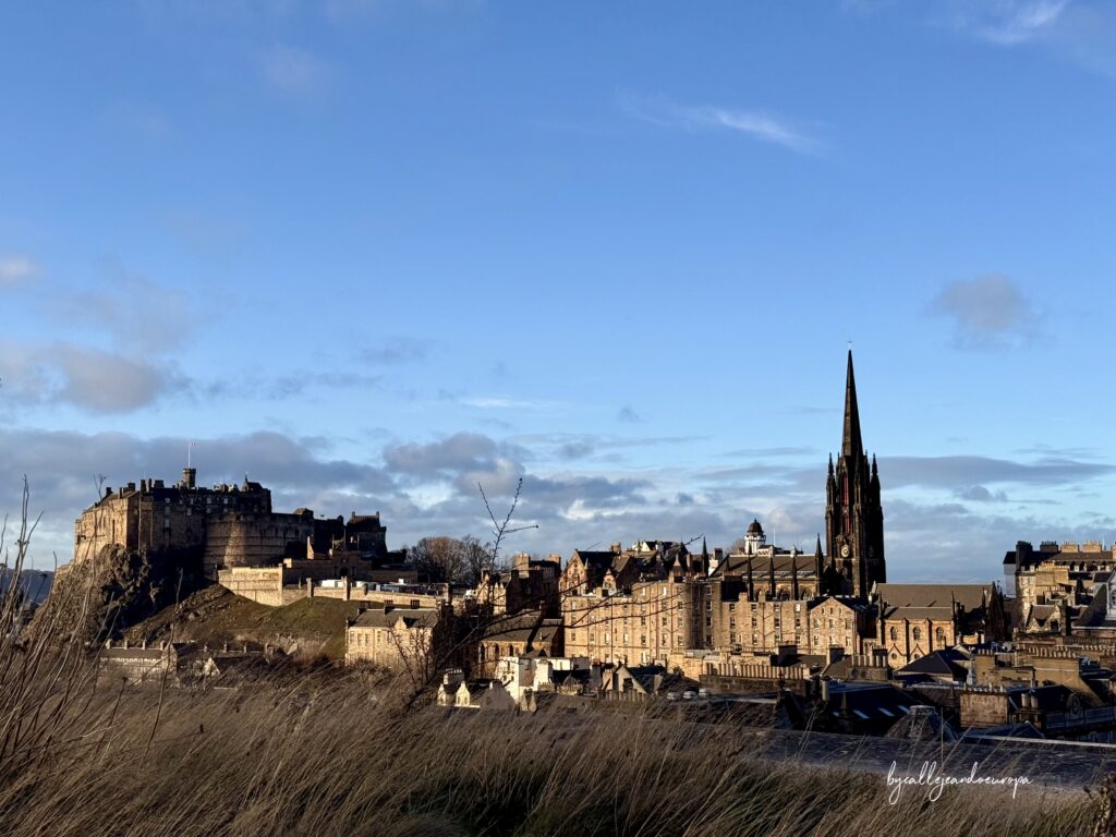 Panorámica de Edimburgo desde la terraza del Museo Nacional de Escocia, con el Castillo de Edimburgo y la aguja de The Hub destacando sobre el horizonte bajo un cielo despejado