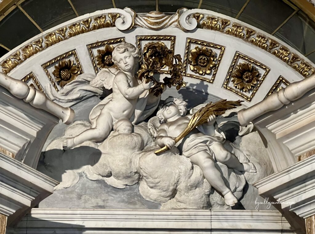 Detalle decorativo de un altar en la Iglesia de Santa Maria in Traspontina, mostrando dos ángeles de estuco blanco sosteniendo una corona y una palma doradas sobre nubes