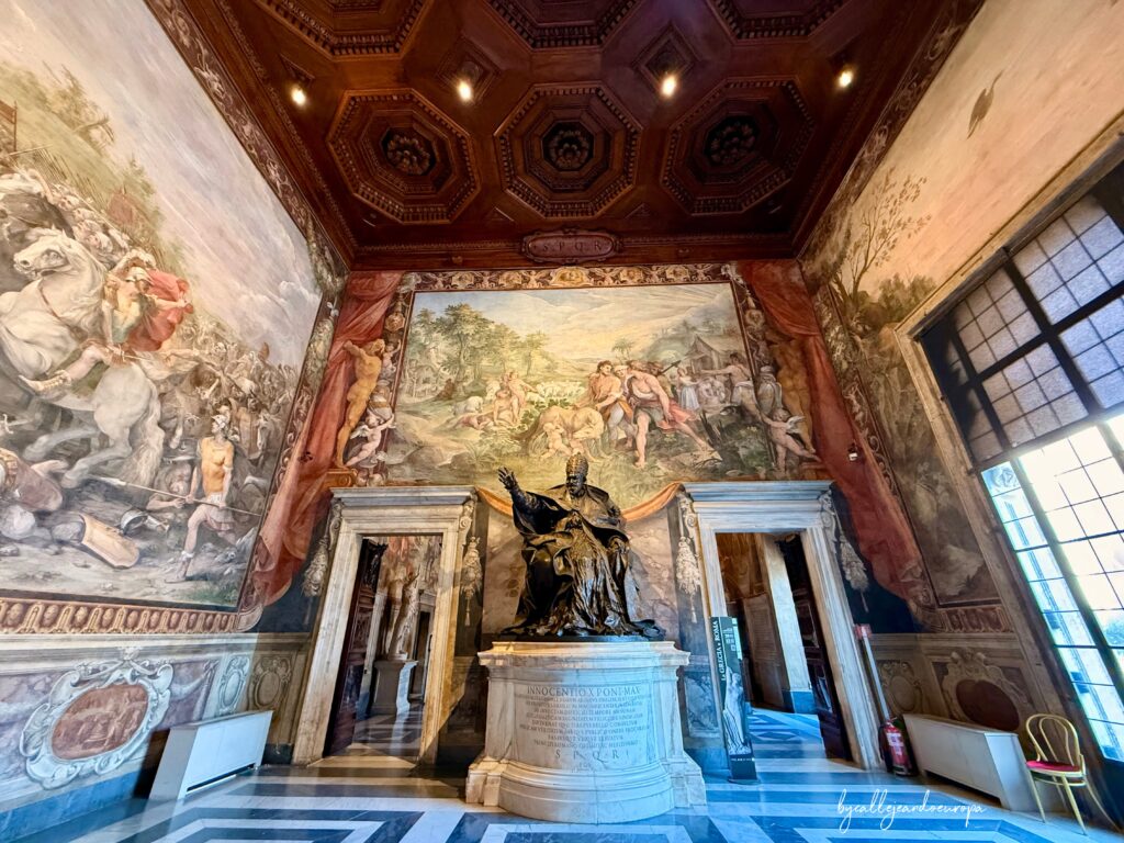 Interior de la Sala de los Horacios y Curiacios en el Palacio de los Conservadores, Museos Capitolinos, mostrando la estatua de Urbano VIII y los frescos barrocos que decoran las paredes y el techo.