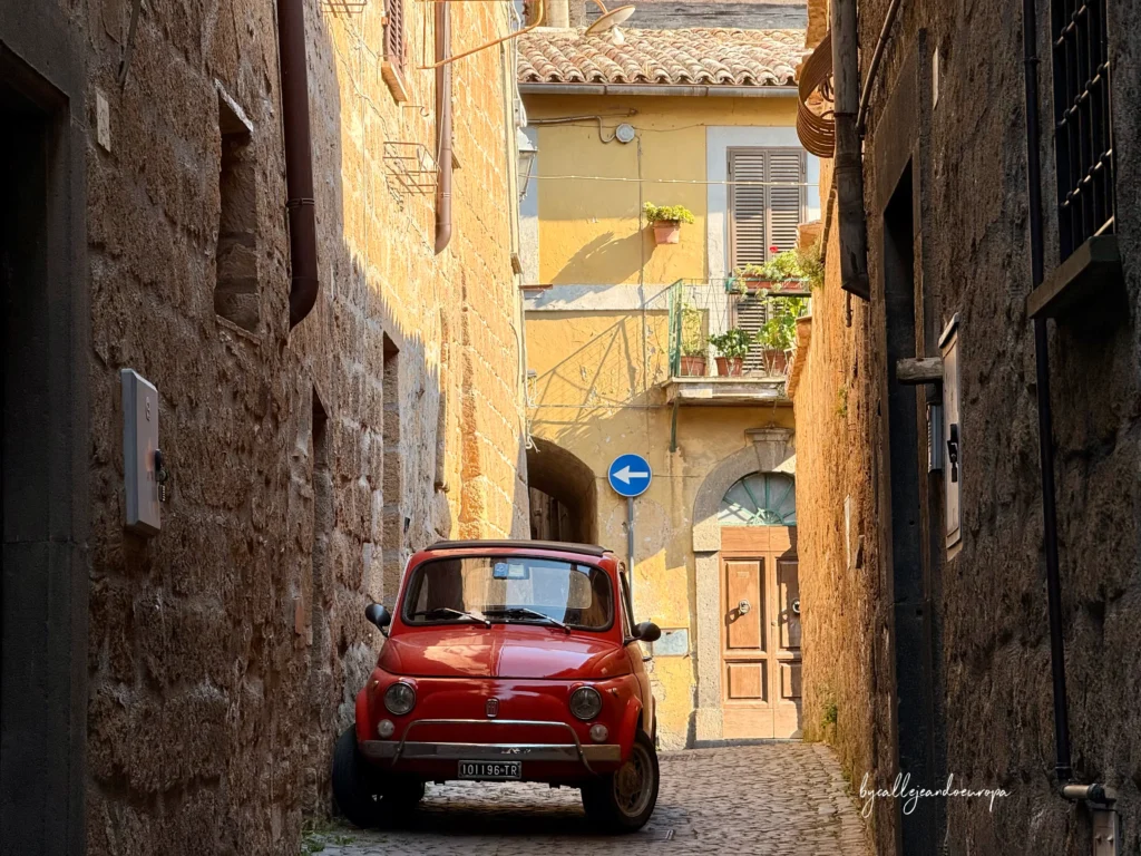 Calle estrecha del casco histórico de Orvieto con un Fiat 600 rojo, una imagen con el encanto tradicional de Umbría, Italia.