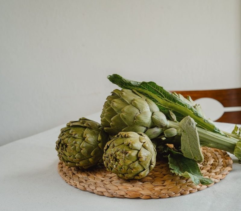 A close-up of fresh artichokes placed on a woven placemat, highlighting natural texture and color.